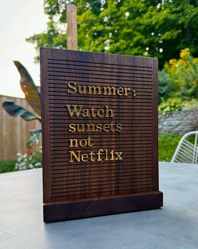 A walnut letter board that reads in gold text: Summer: Watch sunsets not Netflic