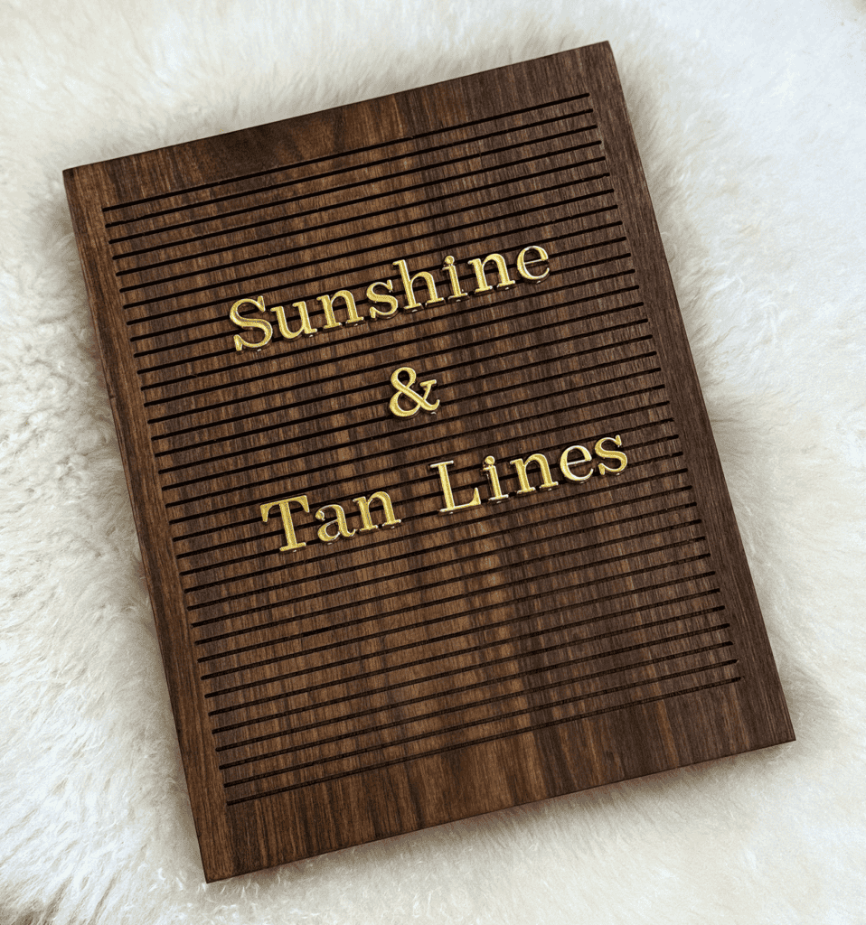 "Sunshine & Tan Lines" in gold serif letters on a dark walnut letter board